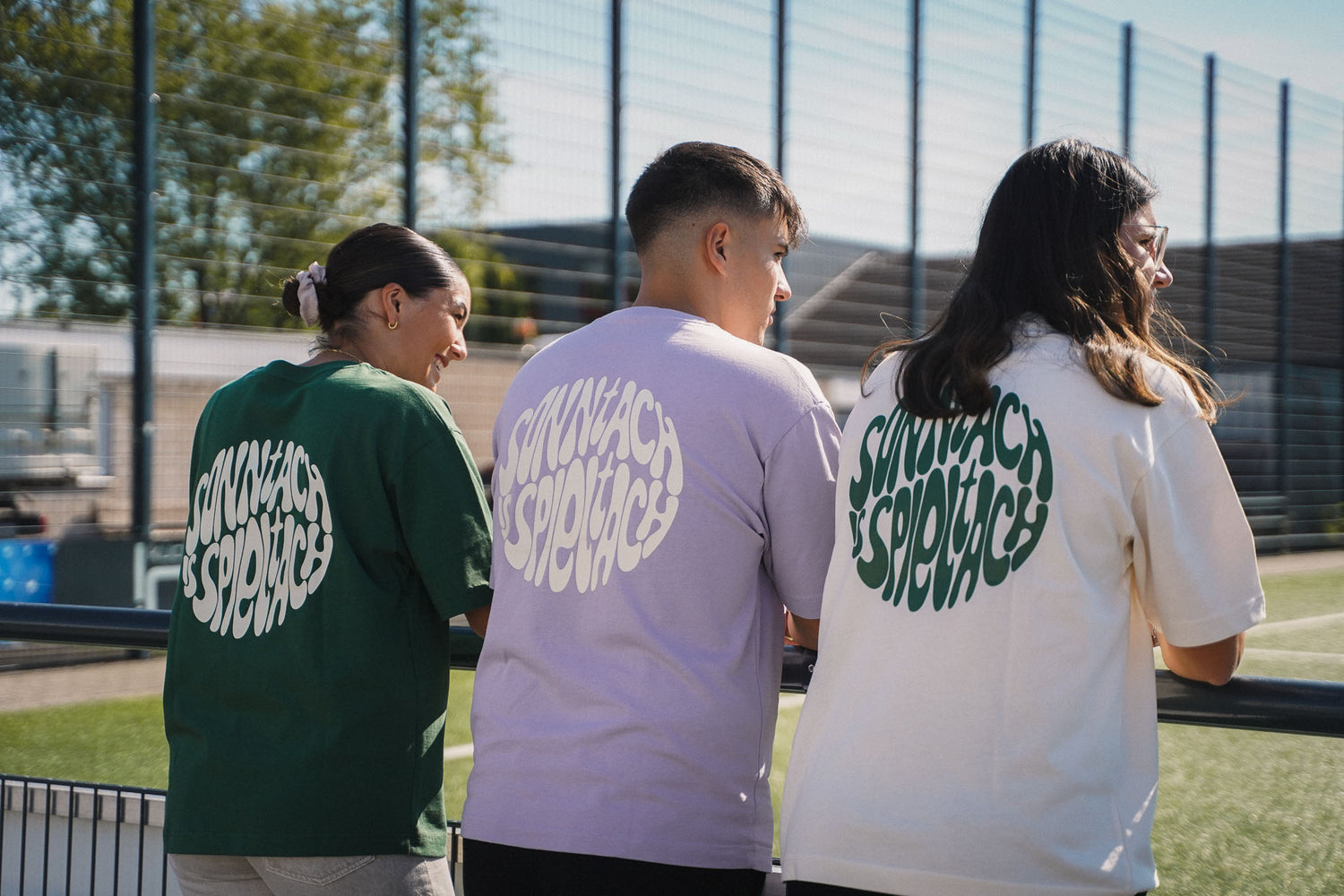 Drei Fußballfans stehen am Seitenrand und schauen ein Spiel. Dabei tragen sie "sonntach is spieltach" Shirts des chapter one in drei Farben.