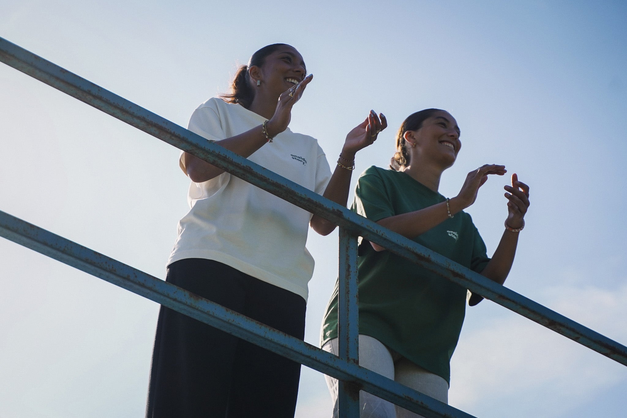 Zwei Fußballfans stehen am Spielfeldrand und applaudieren, während sie das fair produzierte "sonntach is spieltach" Shirt in Cream und Bottlegreen tragen.