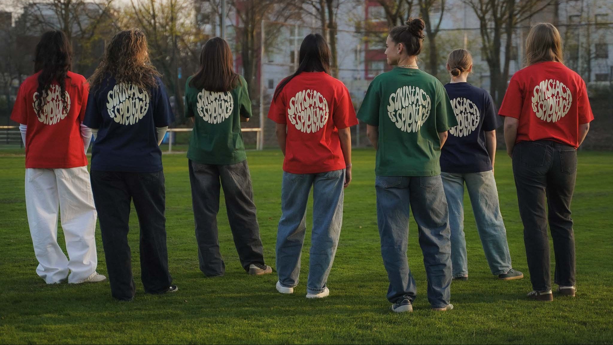 Eine Gruppe junger Frauen stehen auf einem Fußballplatz in der Abendsonne. Alle tragen ein Spieltach Shirt aus Chapter Three.