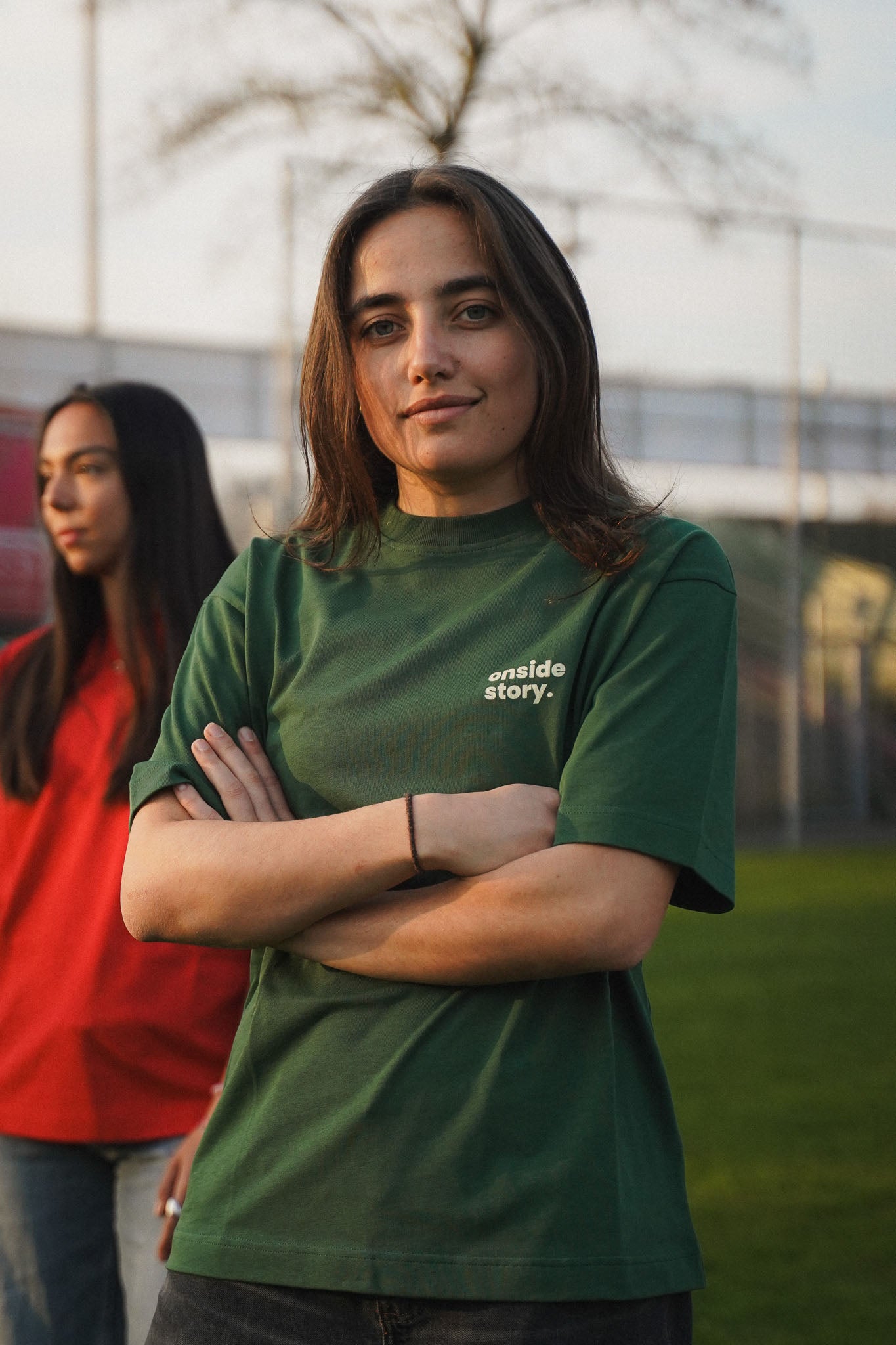 Eine junge Frau steht auf einem Fußballplatz. Sie trägt das Shirt in Bottlegreen aus Chapter Three