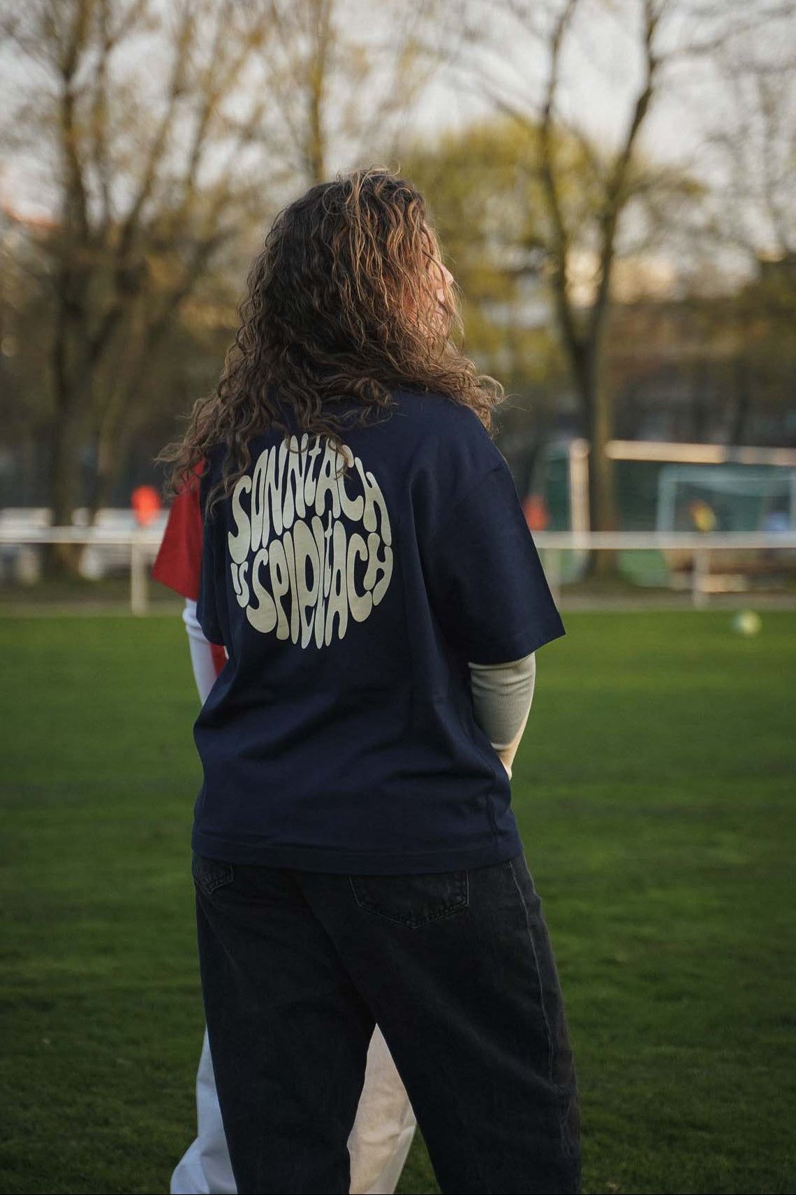 Eine junge Frau steht auf einem Fußballplatz. Sie trägt das "sonntach is spieltach" Shirt in Midnight Blue aus Chapter Three.