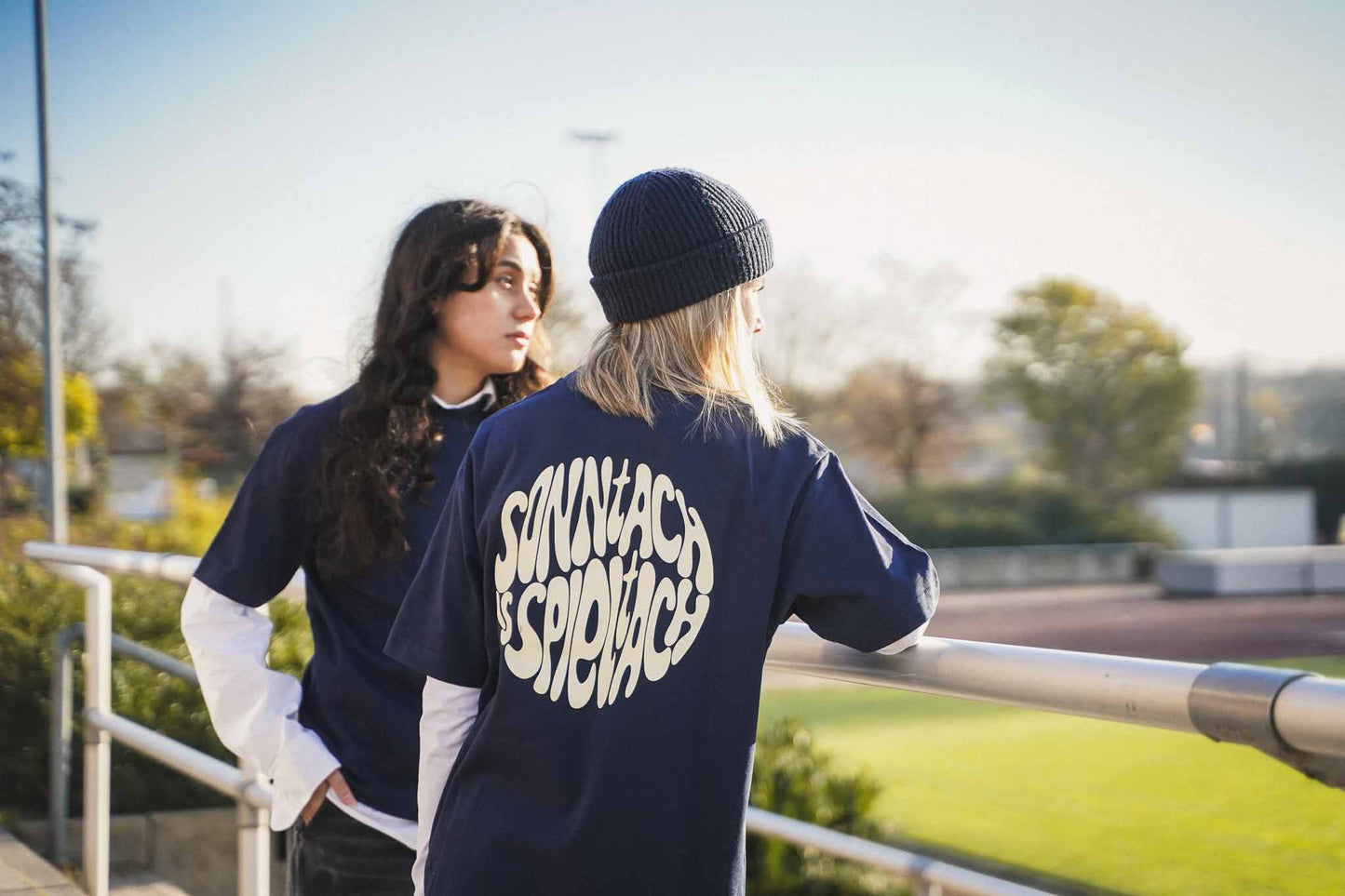 Zwei junge Frauen stehen Spielfeldrand eines Fußballplatzes. Sie tragen das "sonntach is spieltach" Shirt in Midnight Blue in XS.