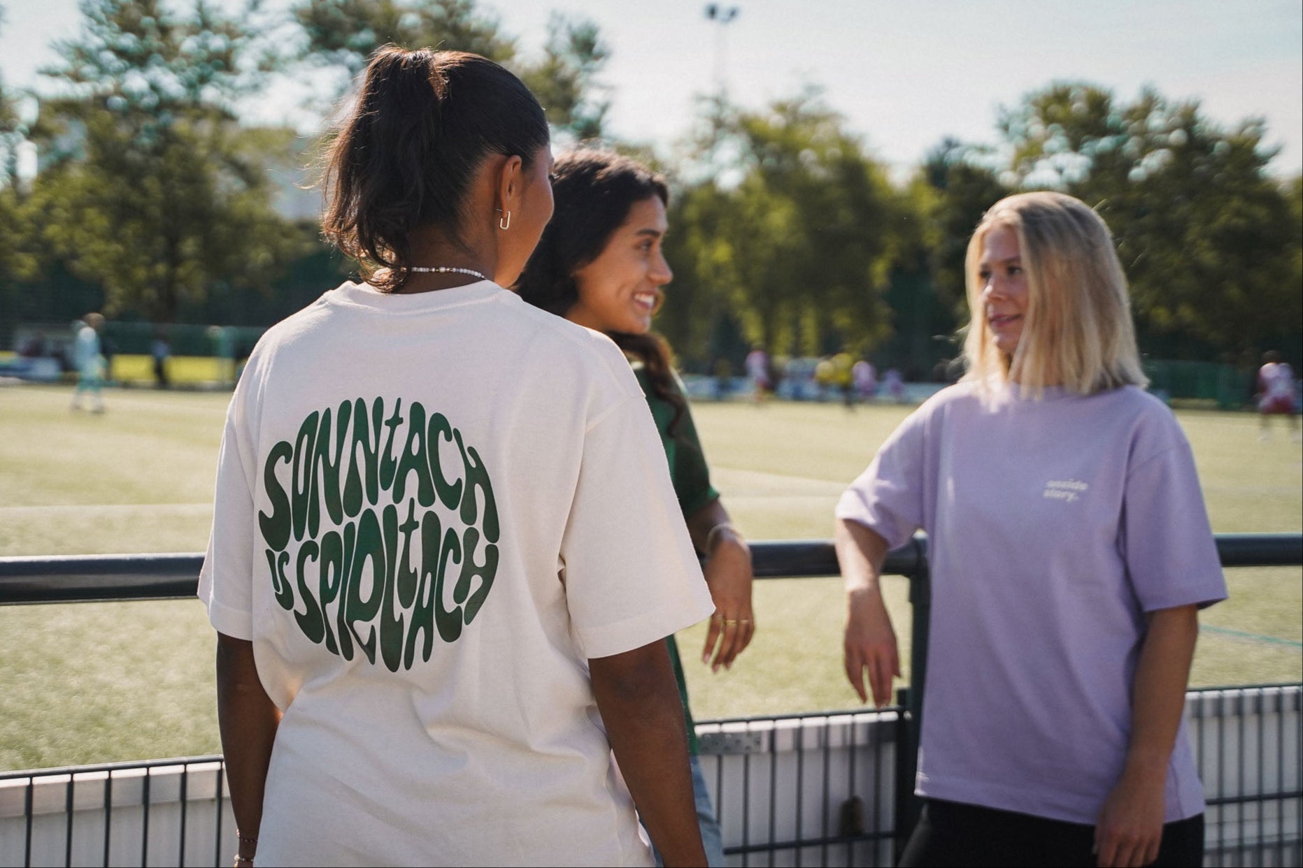 Drei Personen stehen am Spielfeldrand eines Fußballplatzes und tragen onside story Shirts in den Farben Bottlegreen, Cream und Lavender - nachhaltige fair produzierte Streetwear inspiriert vom Fußball.